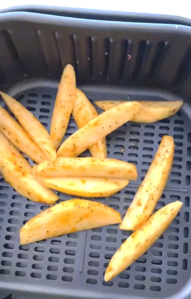 Seasoned raw potato wedges in the air fryer basket